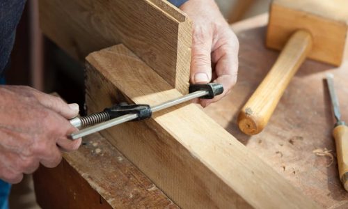 Cropped image of senior male carpenter's hands using screw clamp on wood at workshop